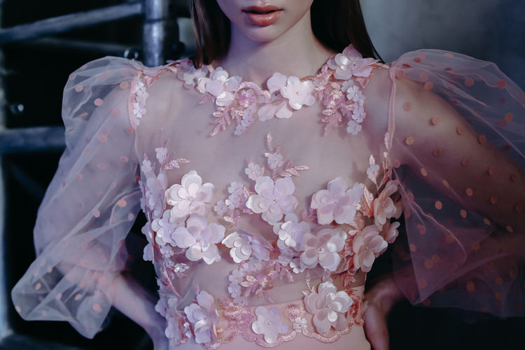 Cropped figure of young beautiful model wearing pink fashion dress with flowers
