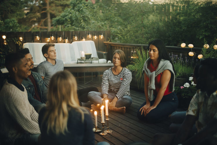 Male and female friends sitting with eyes closed around lit candles in balcony during group therapy session