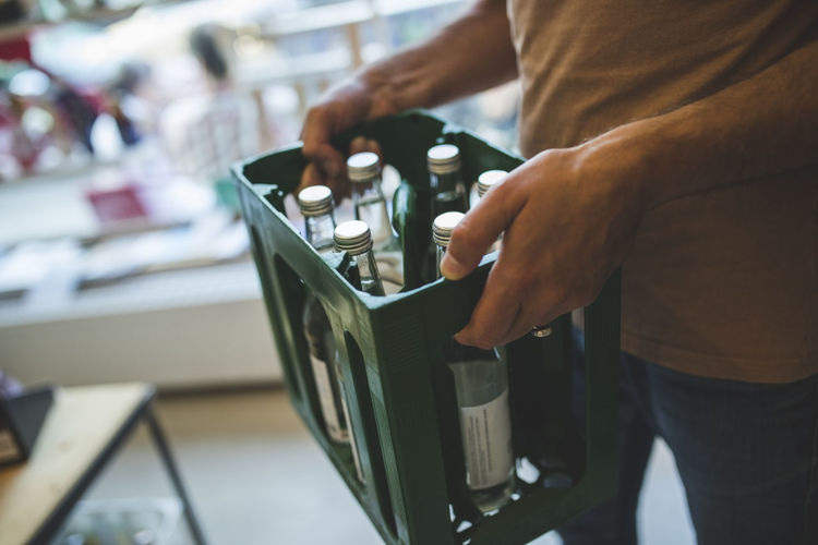 Midsection of salesman carrying bottles in crate at deli