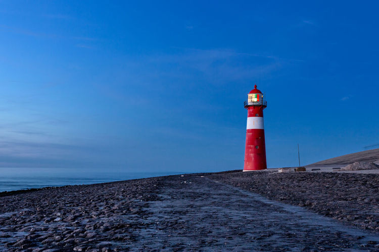 Lighthouse at sea shore against blue sky