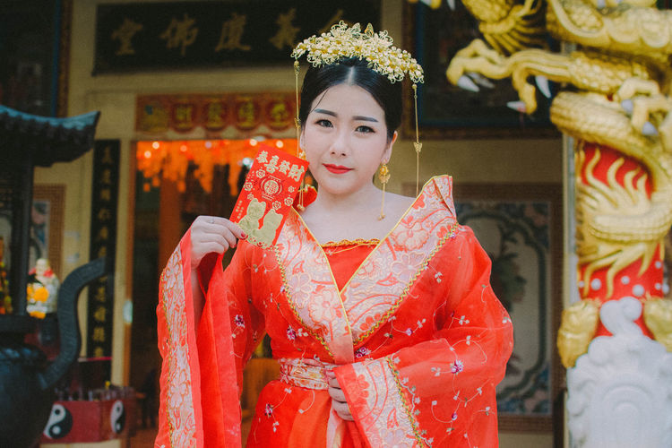Portrait of young woman wearing traditional clothing standing against temple