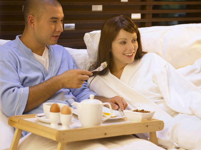 Smiling mid adult couple with food looking away bed at home
