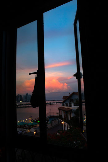 Silhouette buildings against sky during sunset seen through window