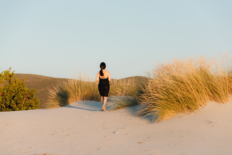 Rear view of woman walking on sand at beach