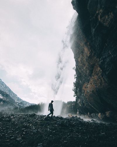 Low angle view of man walking by waterfall against sky