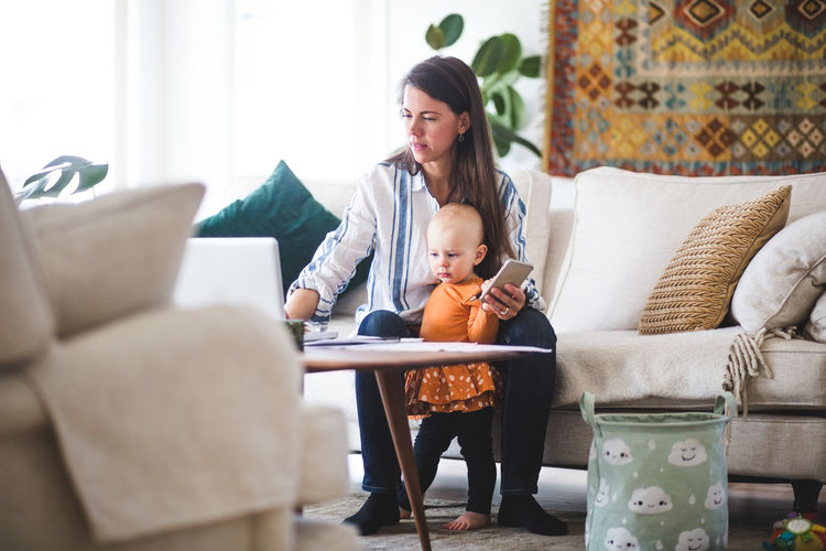 Multi-tasking mother using laptop while taking care of daughter in living room