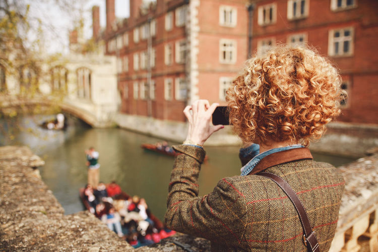 Rear view of young woman photographing while standing on bridge over canal