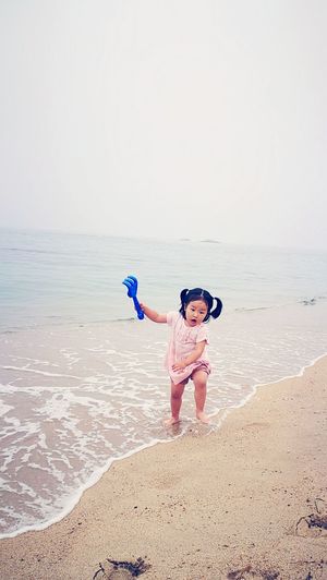Girl holding toy rake while running on shore at beach against sky