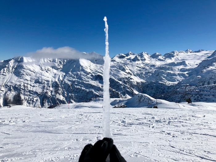 Cropped hand holding icicle against snowcapped mountains