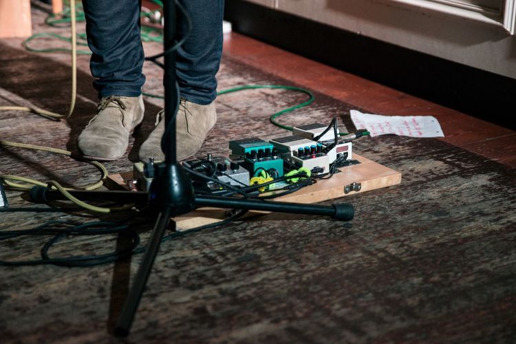 Low section of musician standing by guitar effects pedal on floor