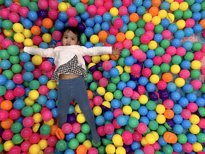 High angle view portrait of girl lying with arms outstretched in ball pool