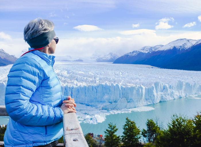Side view of woman standing by railing against glacier