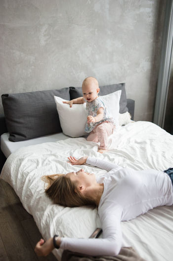 Young woman and baby girl lie on bed and smile while playing. nanny.