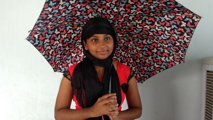 Smiling woman holding umbrella while standing against wall at home