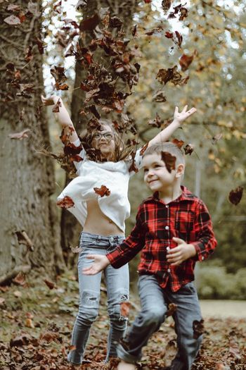 Siblings playing with dry leaves during autumn