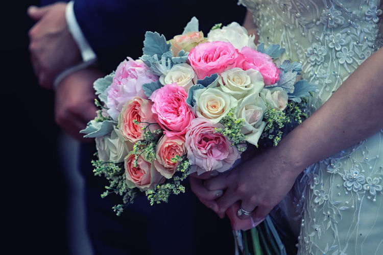 Midsection of bride with rose bouquet standing by groom during wedding ceremony
