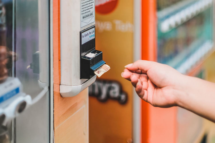 Close-up of hand collecting paper currency dispensing from machine