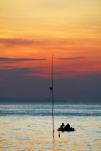 Silhouette people fishing in sea against orange sky