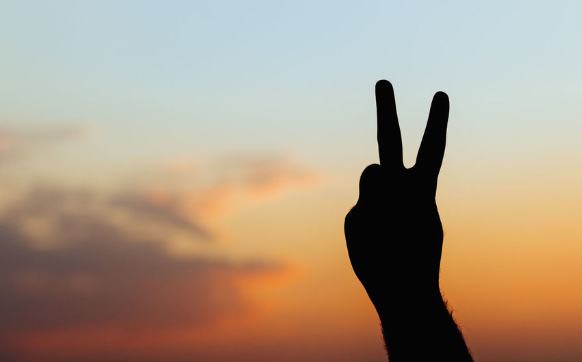 Man's hand isolated on sky background - peace gesture silhouette
