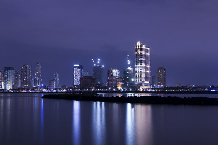 Illuminated buildings by lake in city at night