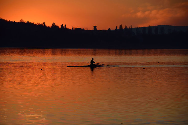 Silhouette man on boat in lake against sky during sunset