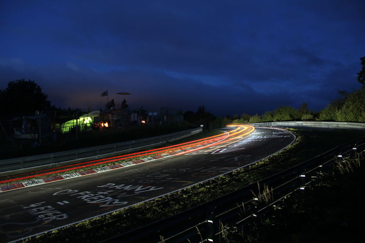 Light trails over street against cloudy sky at night