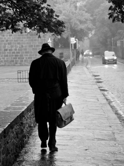 Rear view of man walking on footpath in city during rainy season