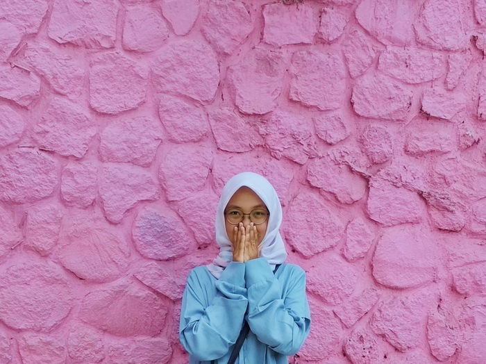 Portrait of woman wearing hijab covering mouth against pink wall