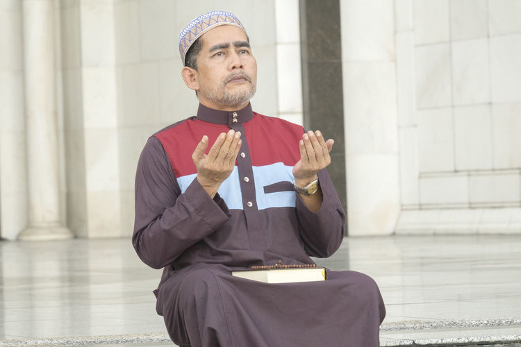 Mature man praying while sitting at mosque