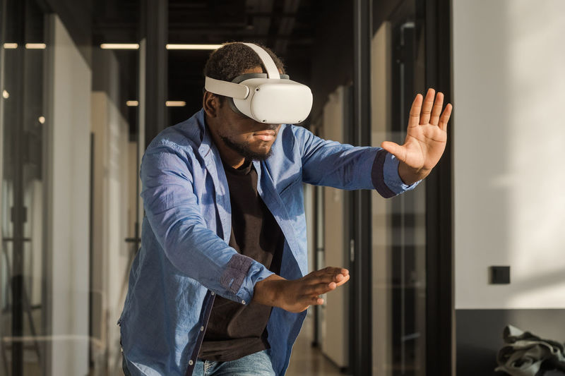 Black man in vr headset exploring metaverse world, touching virtual reality subjects. cyber world