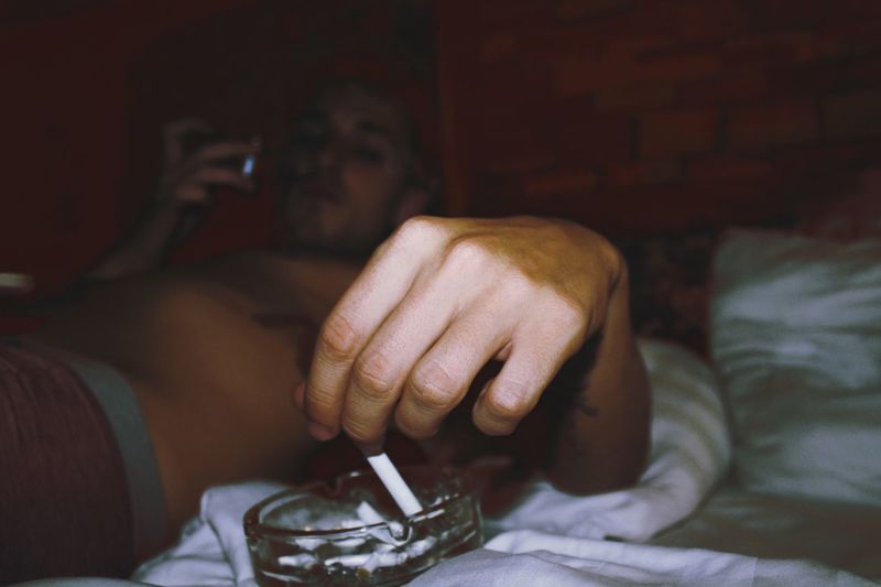 Man smoking cigarette while relaxing on bed