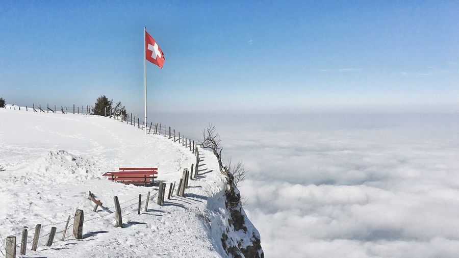 Swiss flag on snow covered mountain by cloudscape