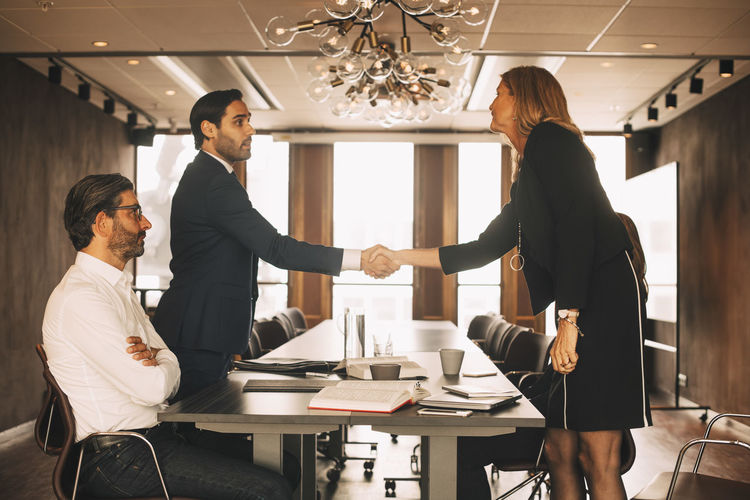 Male and female lawyers shaking hands in board room at office