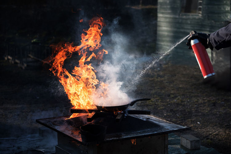 Close-up of cropped hand extinguishing fire on barbecue grill