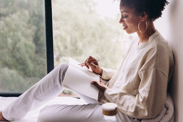 Side view of woman with a smile, writing in a notebook 