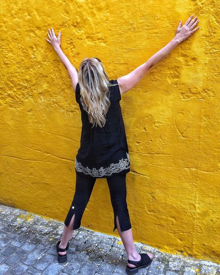 Rear view of woman standing against yellow stone wall
