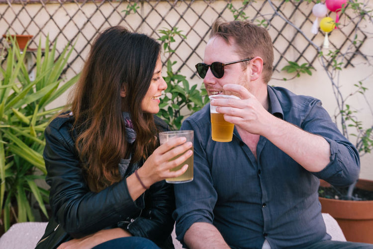 Couple toasting beer glasses while sitting outdoors