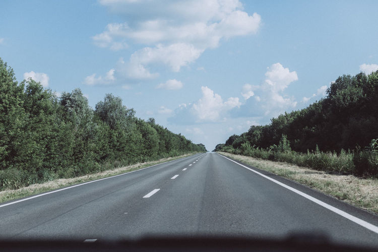 Road by trees against sky seen through car windshield