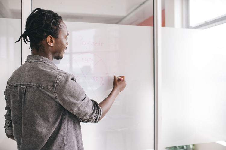 Side view of businessman writing on board in office