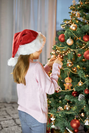 A girl in a santa hat decorates a christmas tree for the new year or christmas. decorating. 