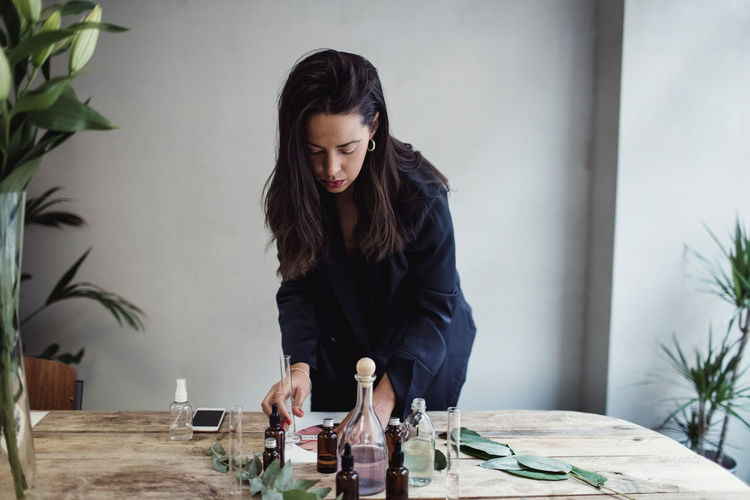 Mid adult female entrepreneur preparing perfume on table against wall at workshop