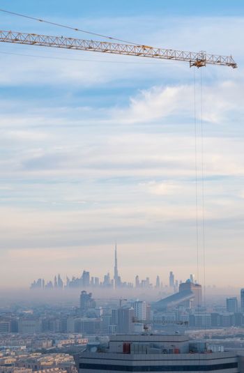 View of crane over cityscape against cloudy sky