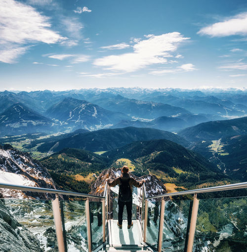Man standing on footbridge over mountains against sky
