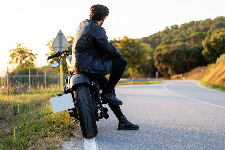 Rear view of bearded man sitting on a motorbike, while looking a¡way to road