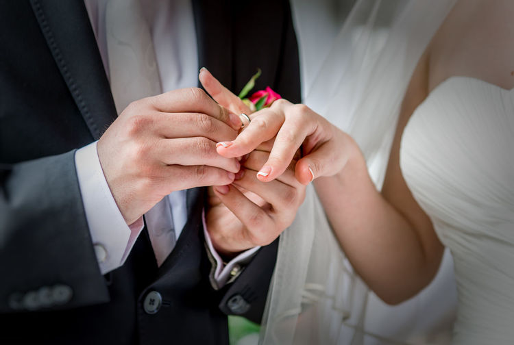 Midsection of groom putting ring in bride finger at wedding
