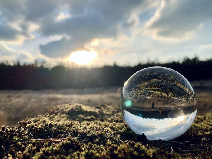 Reflection of crystal ball on glass against sky during sunset