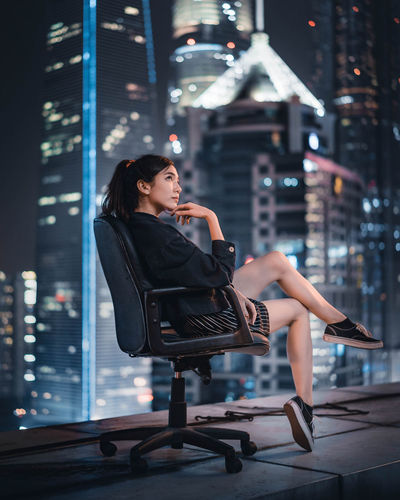 Woman sitting in illuminated city at night