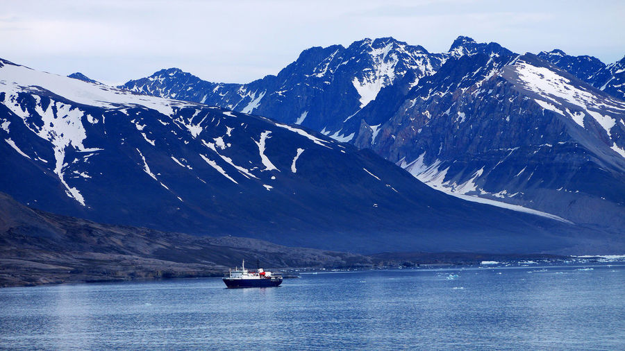 Scenic view of nautical vessel in sea by snowcapped mountains against sky