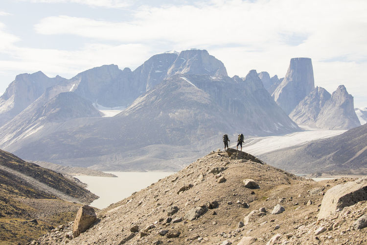 Two hikers stand on high mountain ridge in akshayak pass baffin island