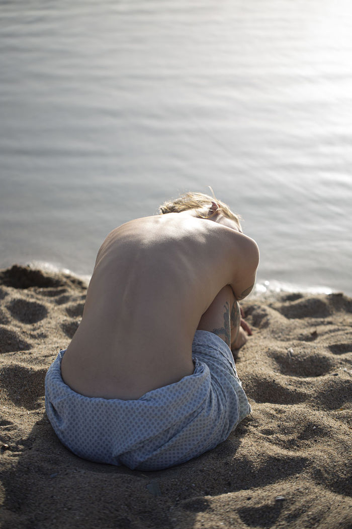 REAR VIEW OF WOMAN RELAXING ON BEACH
